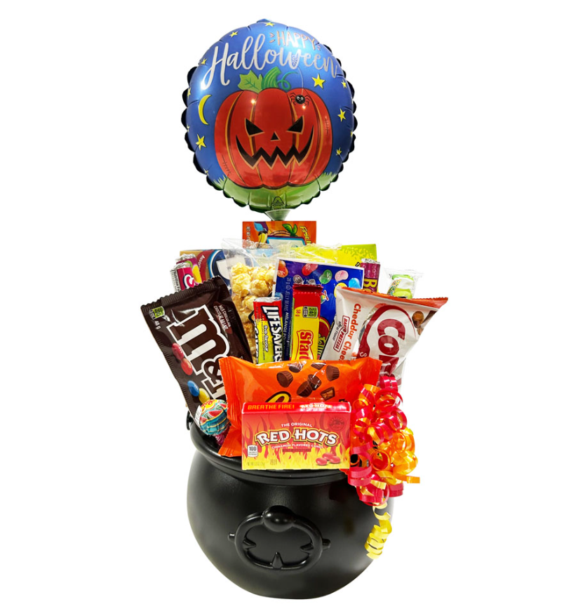 A Halloween-themed candy and snack gift basket arranged in a black cauldron-shaped container with a matching round foil balloon above. The assortment includes packaged snacks such as M&M's, Reese's, KitKat, Red Hots, and Oreo, plus a bright orange and yellow candy bouquet, all on a plain white background.