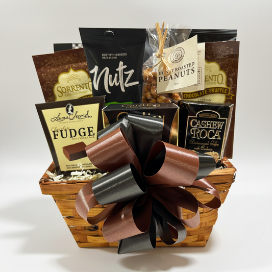 A gourmet chocolate gift basket filled with assorted packaged sweets, including Laura Searls Fudge, Nutz chocolate, and Cashew Rocla chocolate truffles, arranged in a wicker basket with a large brown and black ribbon bow.