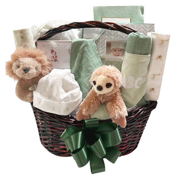 A baby gift basket filled with soft items including a plush sloth toy, a white bonnet, rolled blankets, folded fabrics, and gift boxes, arranged in a dark wicker basket with a large green ribbon bow in front.