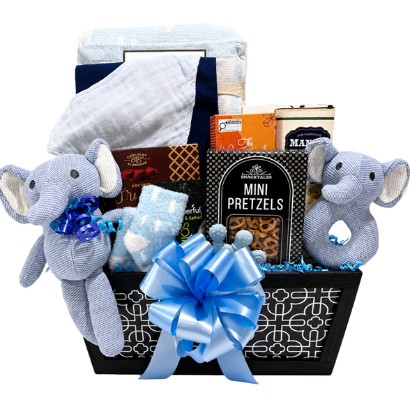 A baby gift basket set against a white background, featuring a black basket with a white geometric pattern and a large blue satin bow. Inside the basket are a light blue and white swaddle blanket, a light blue plush elephant toy with a blue bow on the left, and a matching light blue plush elephant toy on the right.